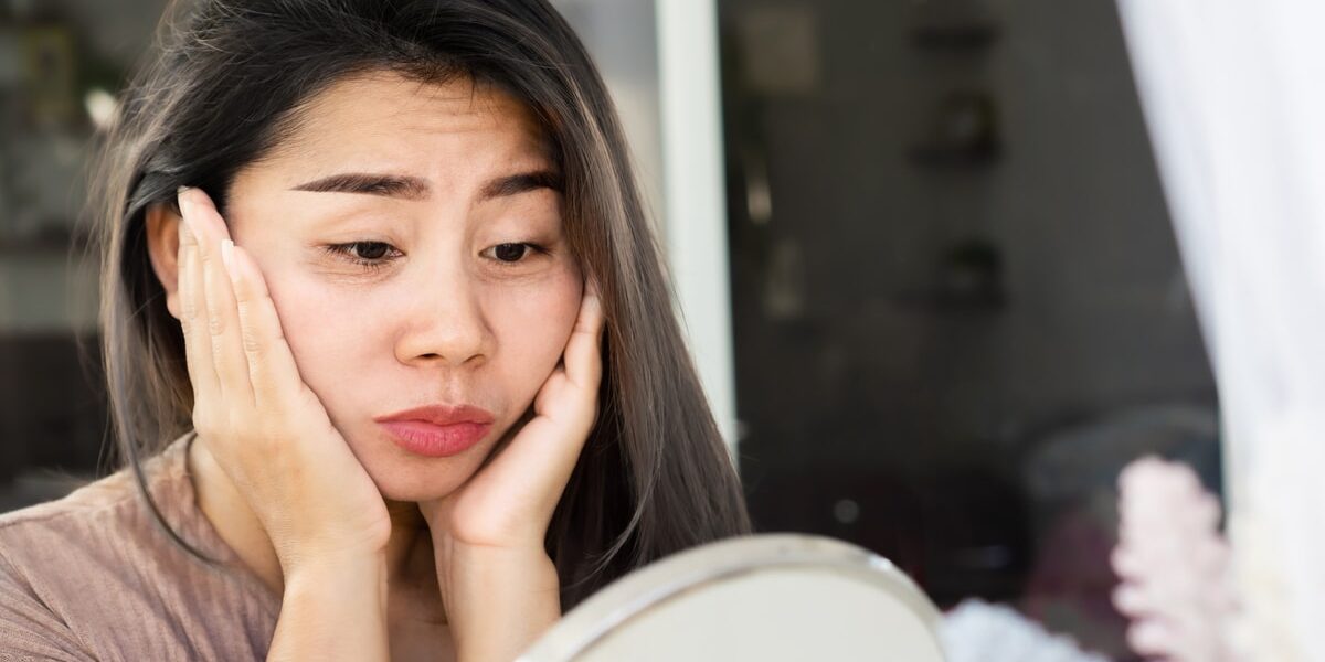 Asian woman checking her eyes bags , dark circles, wrinkle and crow’s feet on her face skin with a mirror Asian woman having problem with eyes bags , dark circles, wrinkle and crow’s feet on her face skin