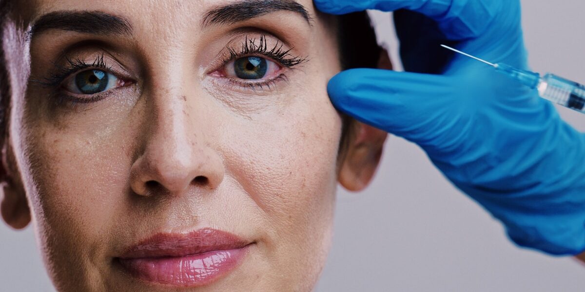 Model, skincare and needle in studio for plastic surgery, relax and antiaging treatment. Mature woman, surgeon hands or injection on white background for cosmetology, transformation or dermal filler Model, skincare and needle in studio for plastic surgery